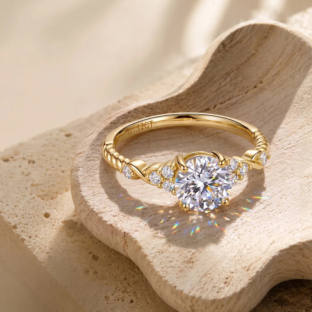 Romantischer Damenring aus 14 Karat vergoldetem Silber mit Zirkonia-Hauptstein und geflochtener Optik auf beiger Deko-Schale