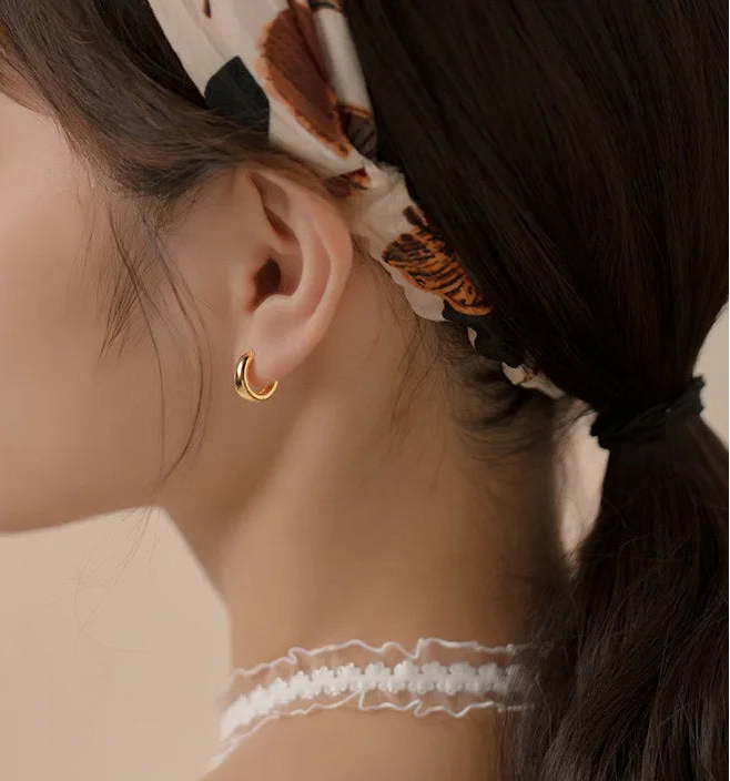 Model trägt kleine, dicke 18K Gold vergoldete Creolen, Haare zurückgebunden, mit goldener Halskette.