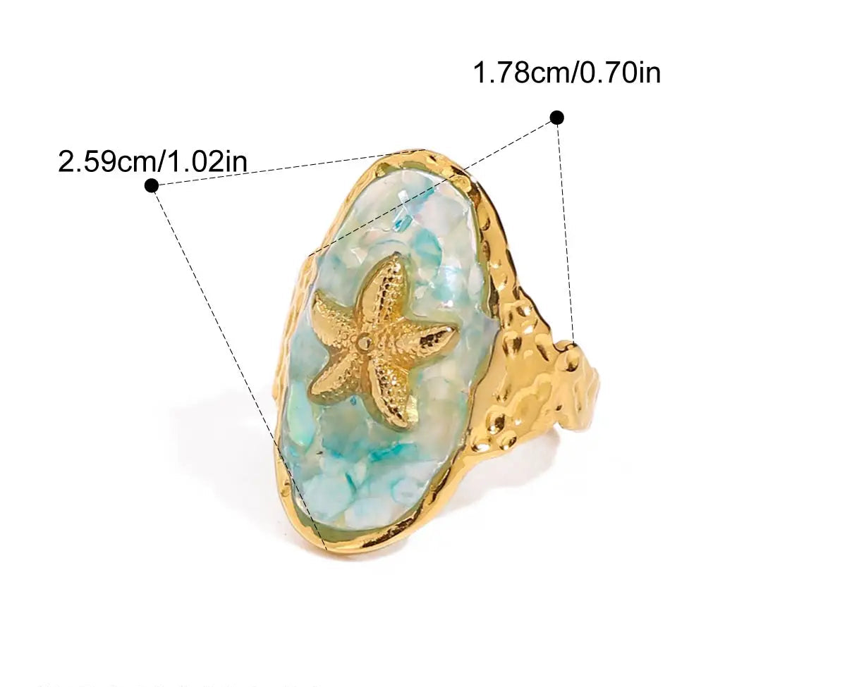 Nahaufnahme eines Rings aus 18K vergoldetem Edelstahl mit einem ovalen, blauen Stein und einem erhabenen Seestern-Symbol. Der Ring hat eine Höhe von 2,6 cm und eine Innendurchmesser von 1,76 cm.