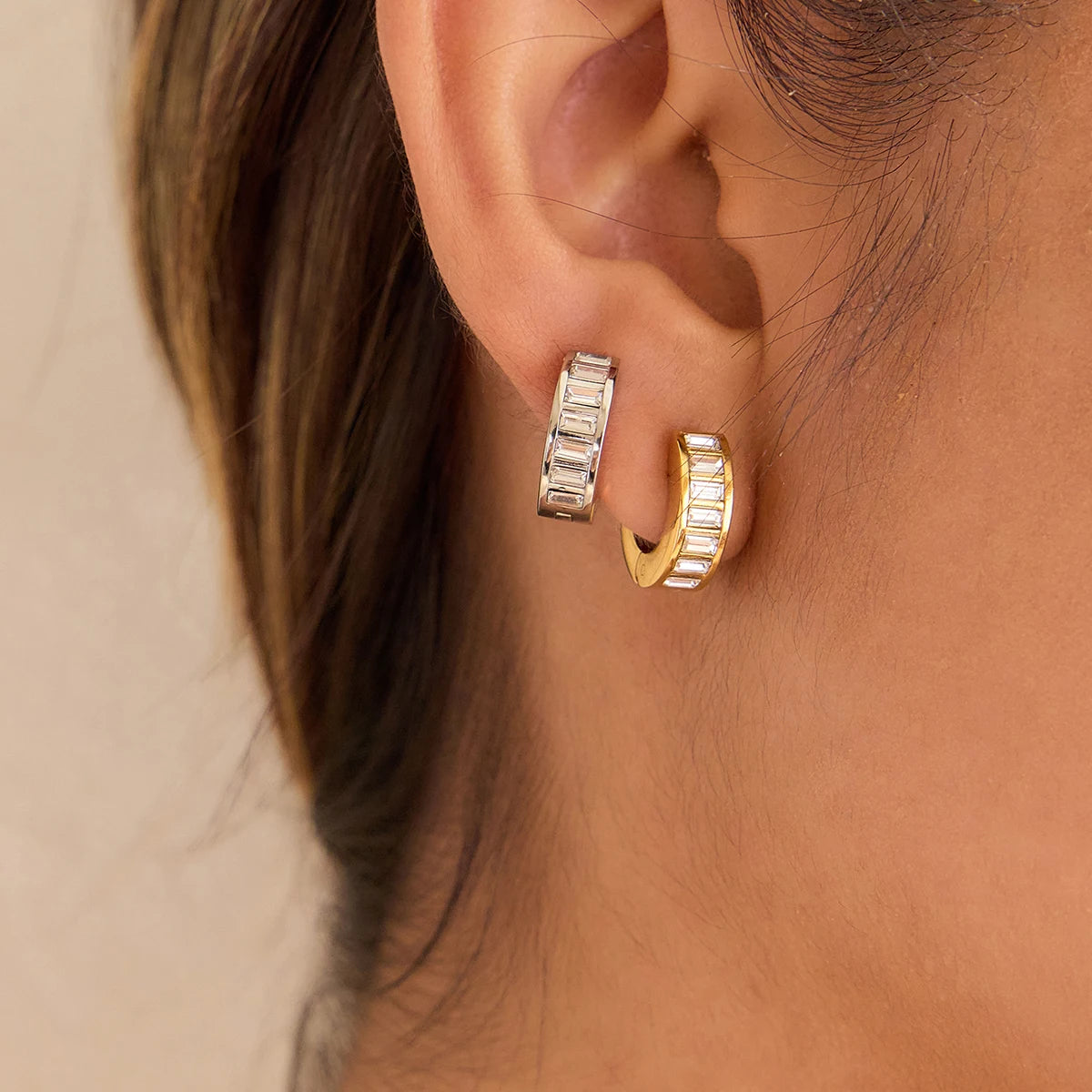 Nahaufnahme der Trägerin, die die 18K goldvergoldete Edelstahl-Huggie-Creole mit klarem Baguette-Zirkonia-Besatz am Ohr zeigt, um die Passform und den Glanz zu demonstrieren.