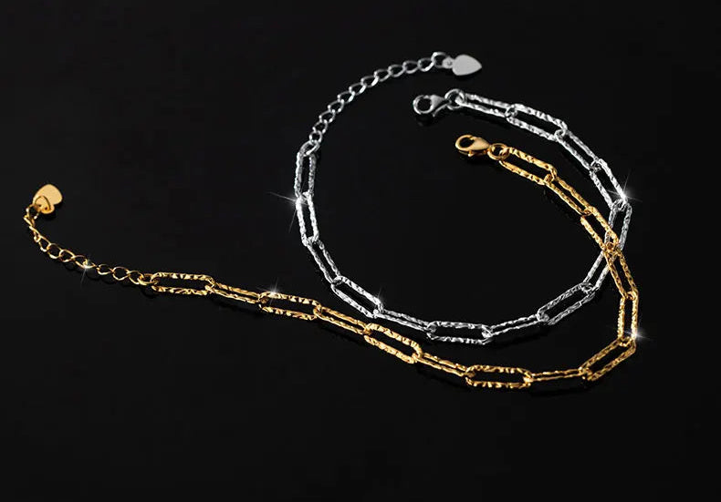 Doppelreihiges Armband/Fußkette, bestehend aus einer feingliedrigen Kette (Silber) und einer länglichen Gliederkette (Goldfarben), liegt spiralförmig auf schwarzem Hintergrund.