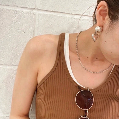 Model mit Sonnenbrille und Halskette, das einen silberfarbenen Kugel-Herz-Ohrring zeigt