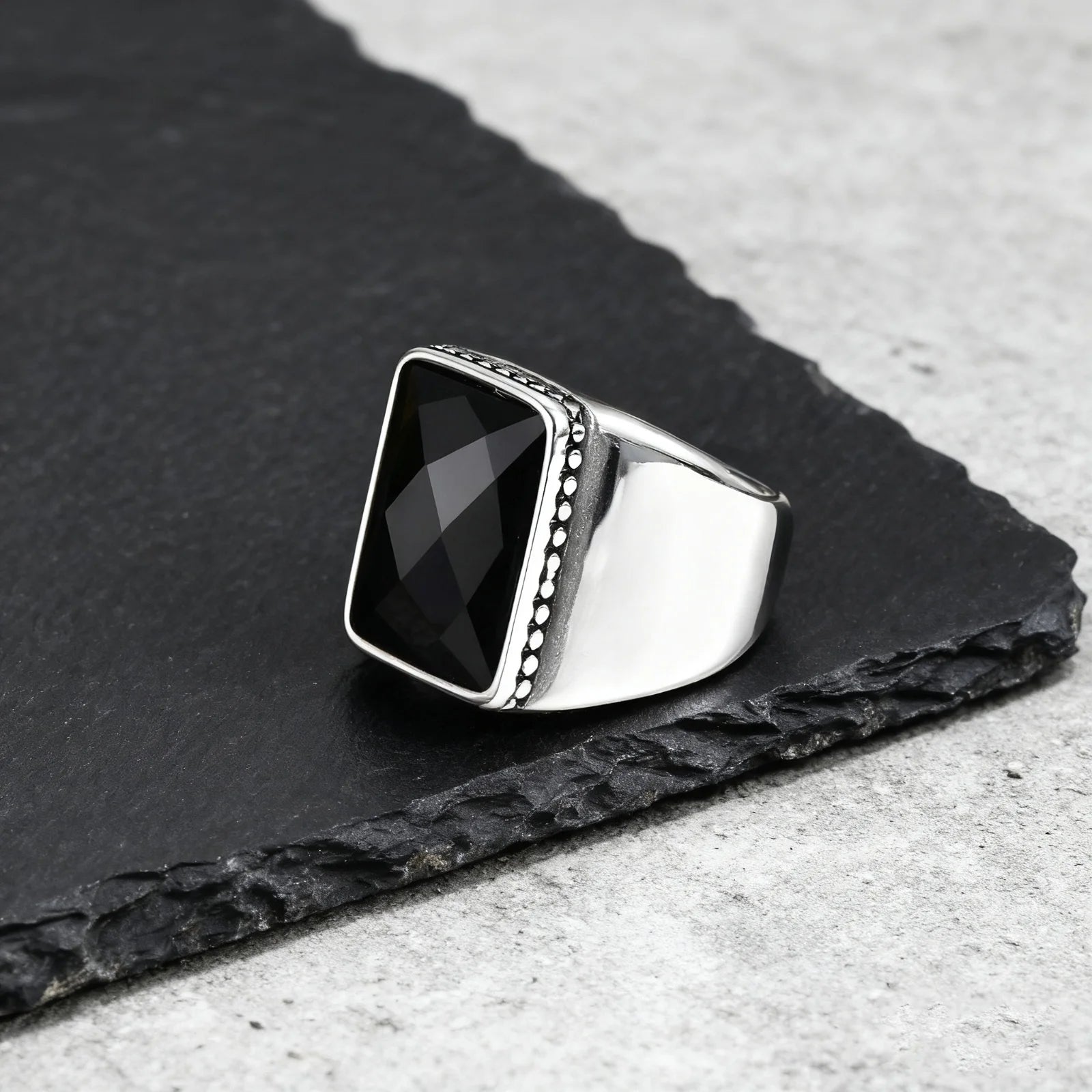 Seitenansicht des maskulinen Edelstahlrings mit glatter, breiter Ringschiene und einer feinen Perlenverzierung um den schwarzen Stein.