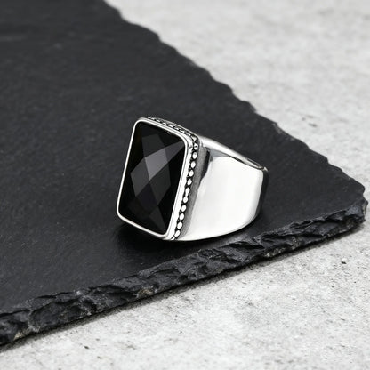 Seitenansicht des maskulinen Edelstahlrings mit glatter, breiter Ringschiene und einer feinen Perlenverzierung um den schwarzen Stein.