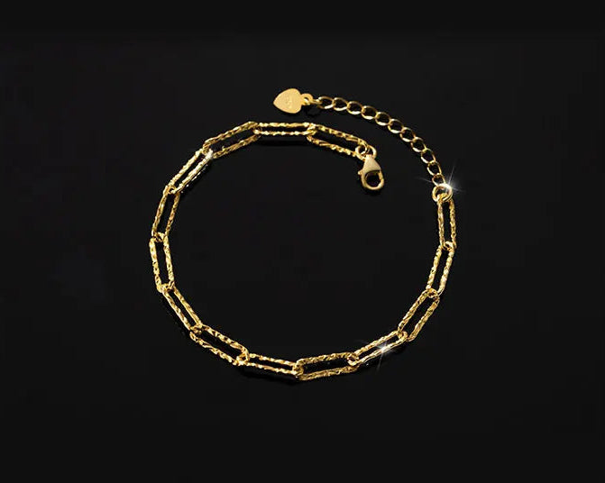 Doppelreihiges Armband/Fußkette, bestehend aus einer feingliedrigen Kette (Schwarz/Silber) und einer länglichen Gliederkette (Goldfarben), liegt spiralförmig auf schwarzem Hintergrund. Es ist ein verstellbarer Verschluss sichtbar.