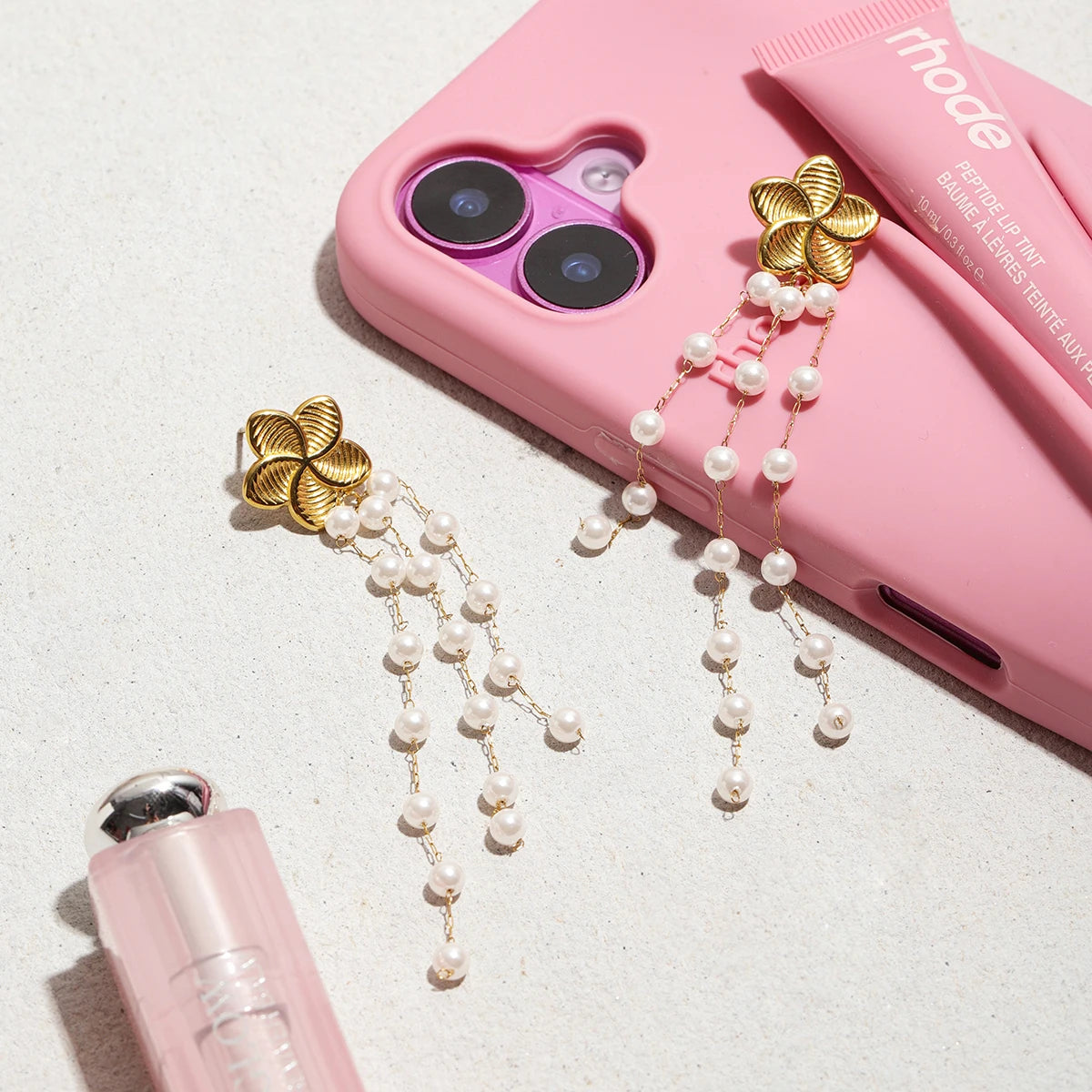 Ein Paar Blumen-Ohrhänger aus 18K vergoldetem Edelstahl mit Acrylperlen, auf einer pinken Handyhülle liegend.