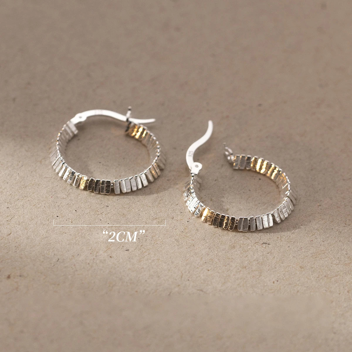 Zwei strukturierte Kreolen-Ohrringe (925er Silber) liegen nebeneinander, mit einem sichtbaren Maßband zur Größenbestimmung.

