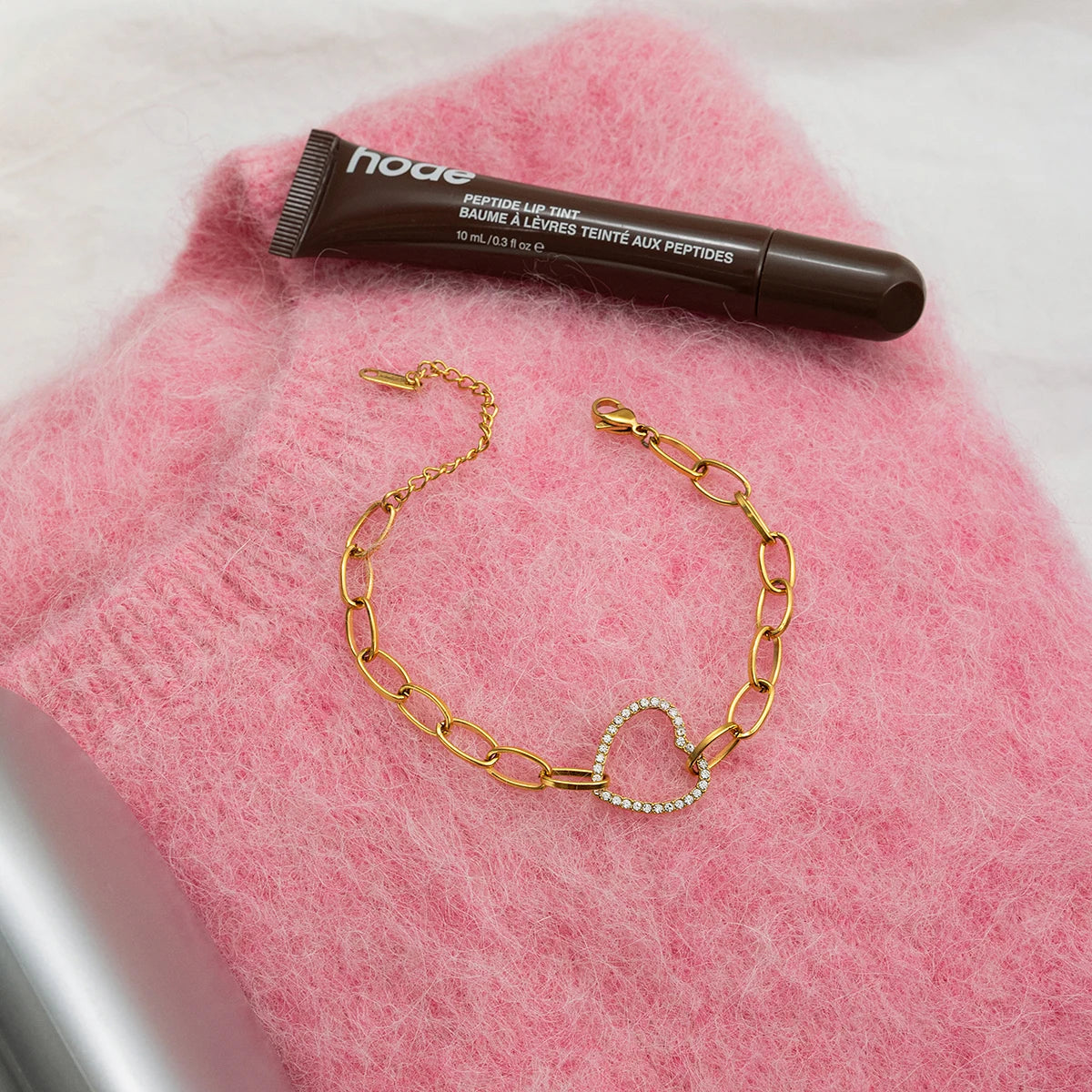 Gliederarmband aus vergoldetem Edelstahl mit Herz-Charm im Flatlay präsentiert auf einem rosa Flauschpullover