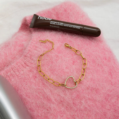 Gliederarmband aus vergoldetem Edelstahl mit Herz-Charm im Flatlay präsentiert auf einem rosa Flauschpullover