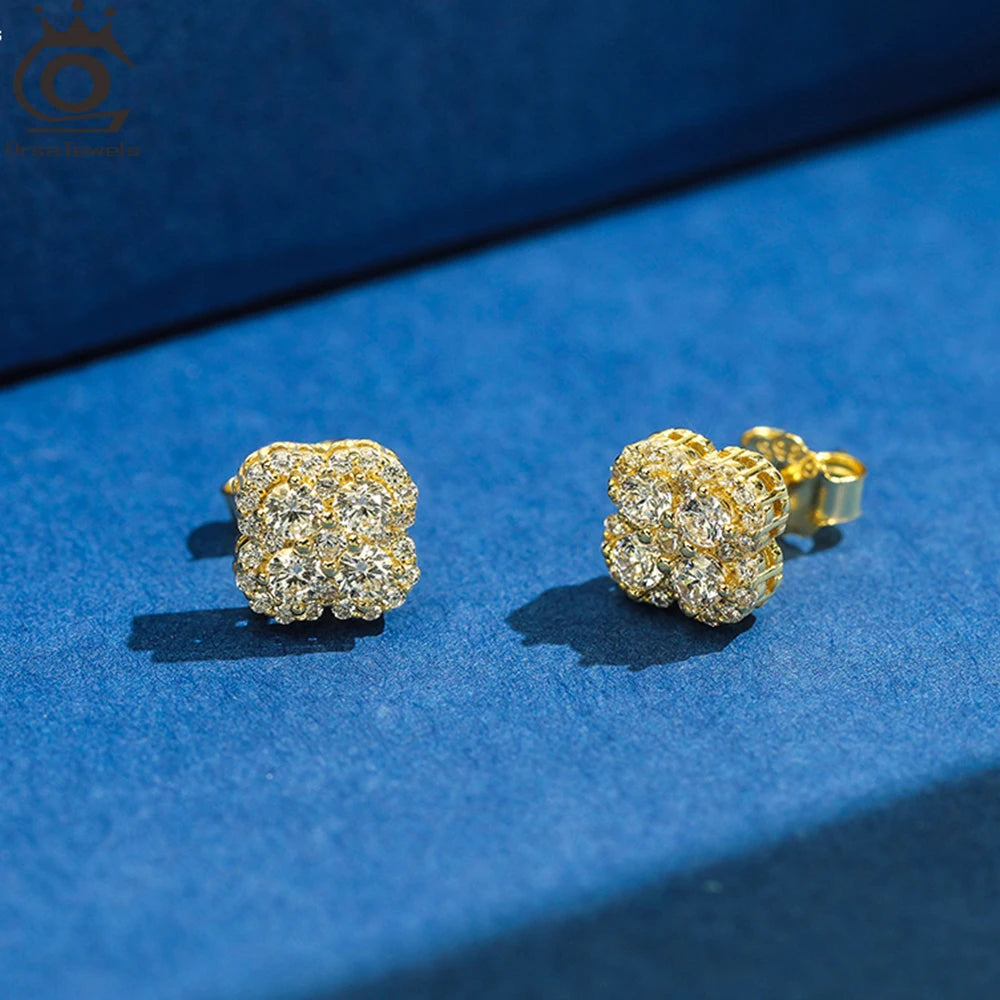 Paar Kleeblatt-Ohrstecker aus 14K vergoldetem 925er Silber, detailreich besetzt mit funkelnden Zirkonia-Steinen, präsentiert auf blauem Untergrund.