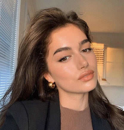 Model mit dunklem Blazer trägt dezente, glänzende 18K Gold Creolen im Alltags-Look.