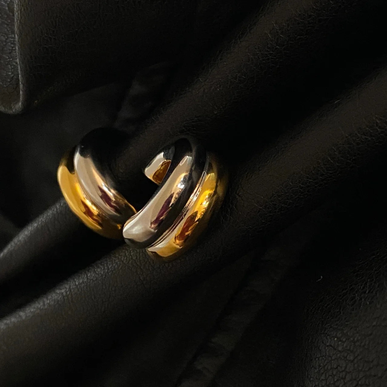 Bi-Color Creolen-Ohrringe aus Messing mit Gold- und Silber-Finish auf schwarzem Stoffuntergrund.