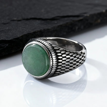 Massiver Herren-Siegelring aus Edelstahl im Vintage-Design mit einem ovalen, grünen Schmuckstein, platziert vor einer dunklen Schieferplatte.