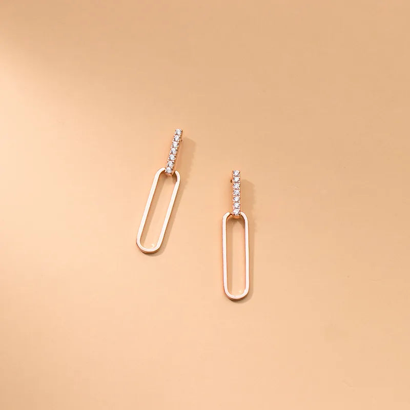 Produktansicht der 18K rosévergoldeten Ohrstecker mit Zirkonia-Steinen und ovalem Ketten-Element auf beigem Grund.