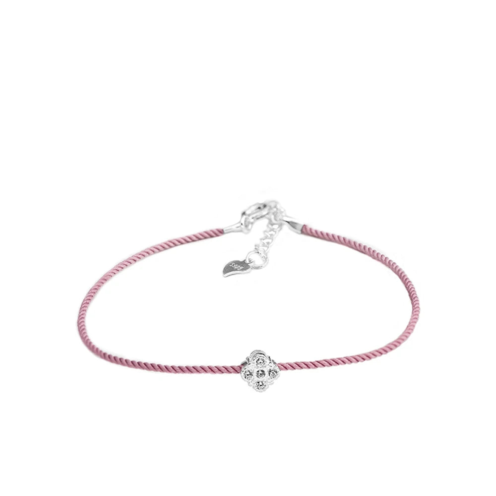 Armband mit zartrosa Textilband und einem kleinen, runden Anhänger aus 925er Silber mit einem zentralen Zirkoniastein. Das Armband hat einen verstellbaren 925er Silber-Verschluss mit einem kleinen Herz-Anhänger.