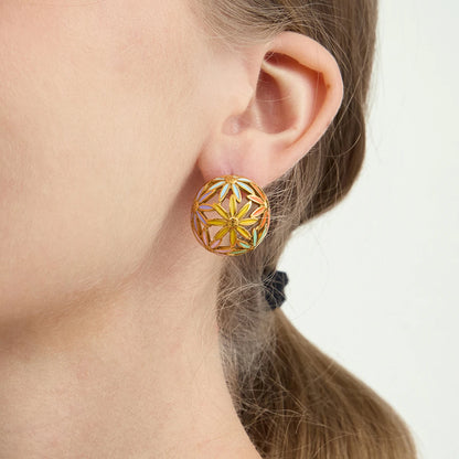 Nahaufnahme einer Frau, die einen großen, vergoldeten Edelstahl-Ohrstecker in floralem Gitter-Design am Ohr trägt.