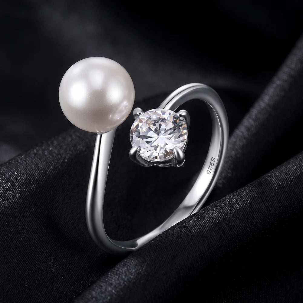 Glänzender offener Perlenring aus 925 Sterling Silber mit rundem Zirkonia und echter Süßwasserperle edel inszeniert auf schwarzem Grund.
