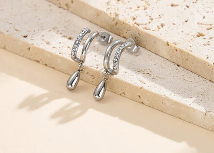Silberfarbene Edelstahl-Ohrringe in doppelter Hoop-Optik mit Zirkonia und Tropfenanhänger auf Naturstein.