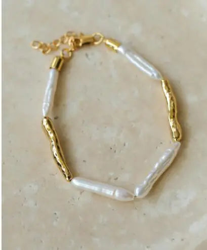 Filigranes Armband aus echten Barockperlen und goldenen Akzenten, präsentiert auf einem minimalistischen hellen Untergrund.