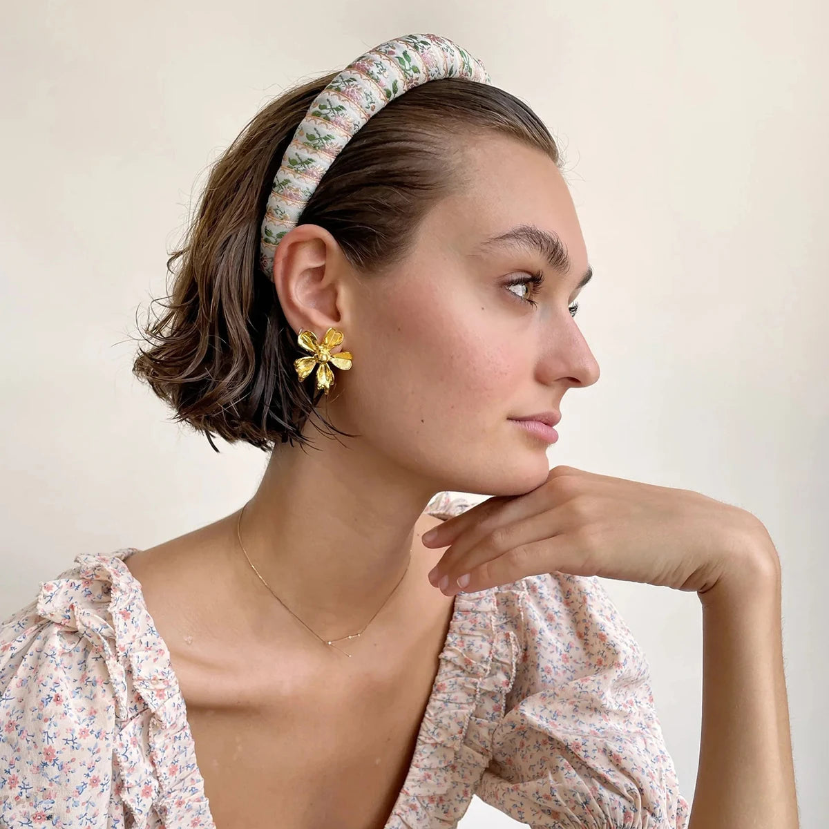Porträt einer Frau mit einem bedruckten Haarband und einem floralen Edelstahl-Statement-Ohrring mit 18K Vergoldung, um das Design direkt am Ohr zu präsentieren.