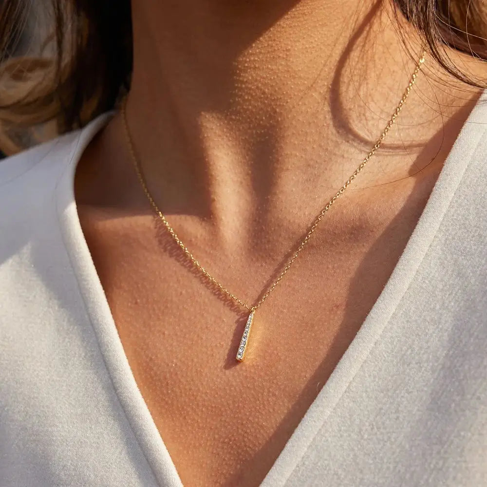 Fokus auf das Dekolleté einer Frau, die die filigrane PVD-goldbeschichtete Edelstahlkette mit dem vertikalen Strass-Anhänger zu einem weißen Oberteil trägt.