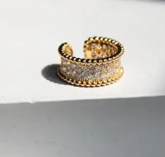 Ein offener Ring aus 18K vergoldetem Messing steht auf einer hellen Fläche; das Sonnenlicht betont die feine Körnung des Goldes und die präzise gefassten Zirkonia-Steine in der Mitte.