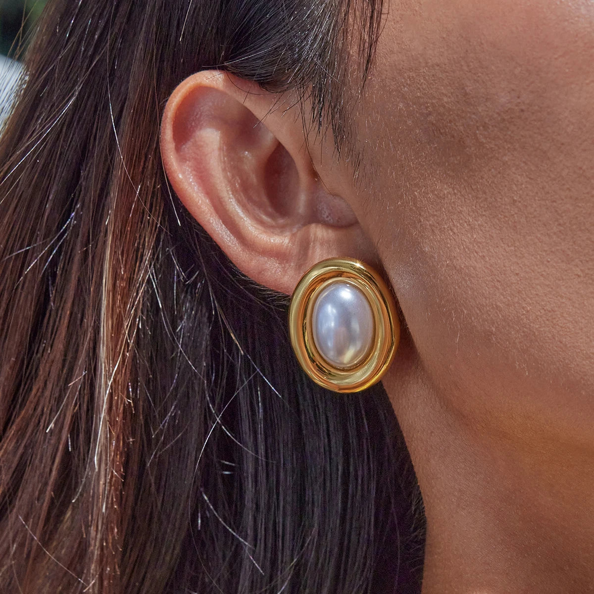Nahaufnahme stilvoller Ohrringe mit einem 18K vergoldeten Edelstahlrahmen und einer großen, glänzenden Harzperle in der Mitte. Die Ohrringe werden von einem Model getragen.