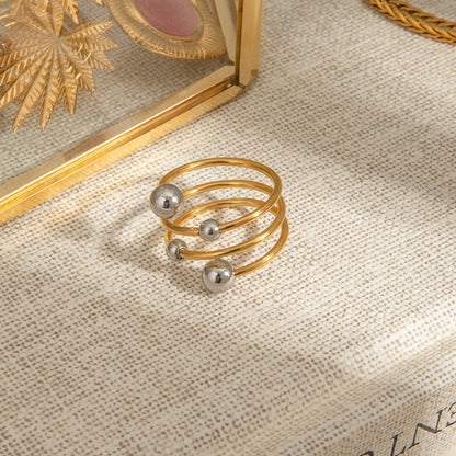 „Minimalistischer Wickelring in Gold und Silber auf natürlichem Hintergrund, ideal für den modernen Layering-Look.“