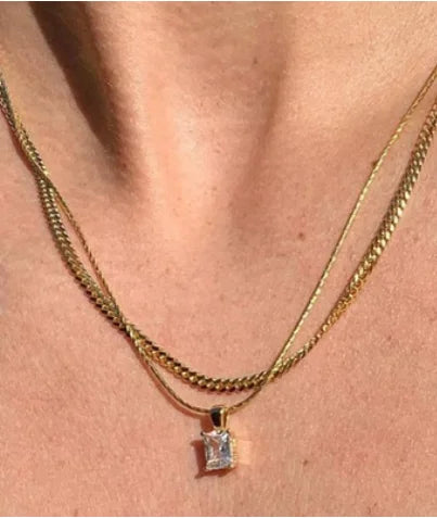 Goldene Kette mit rechteckigem Solitär-Zirkonia-Anhänger, elegant drapiert an einer weißen, wellenförmigen Keramikschale.