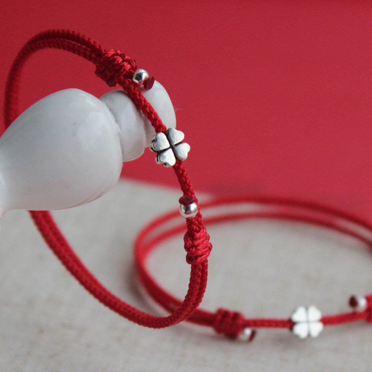 Nahaufnahme eines handgefertigten roten Textilarmbands mit vierblättrigem Kleeblatt und Perlen aus 925er Sterling Silber.