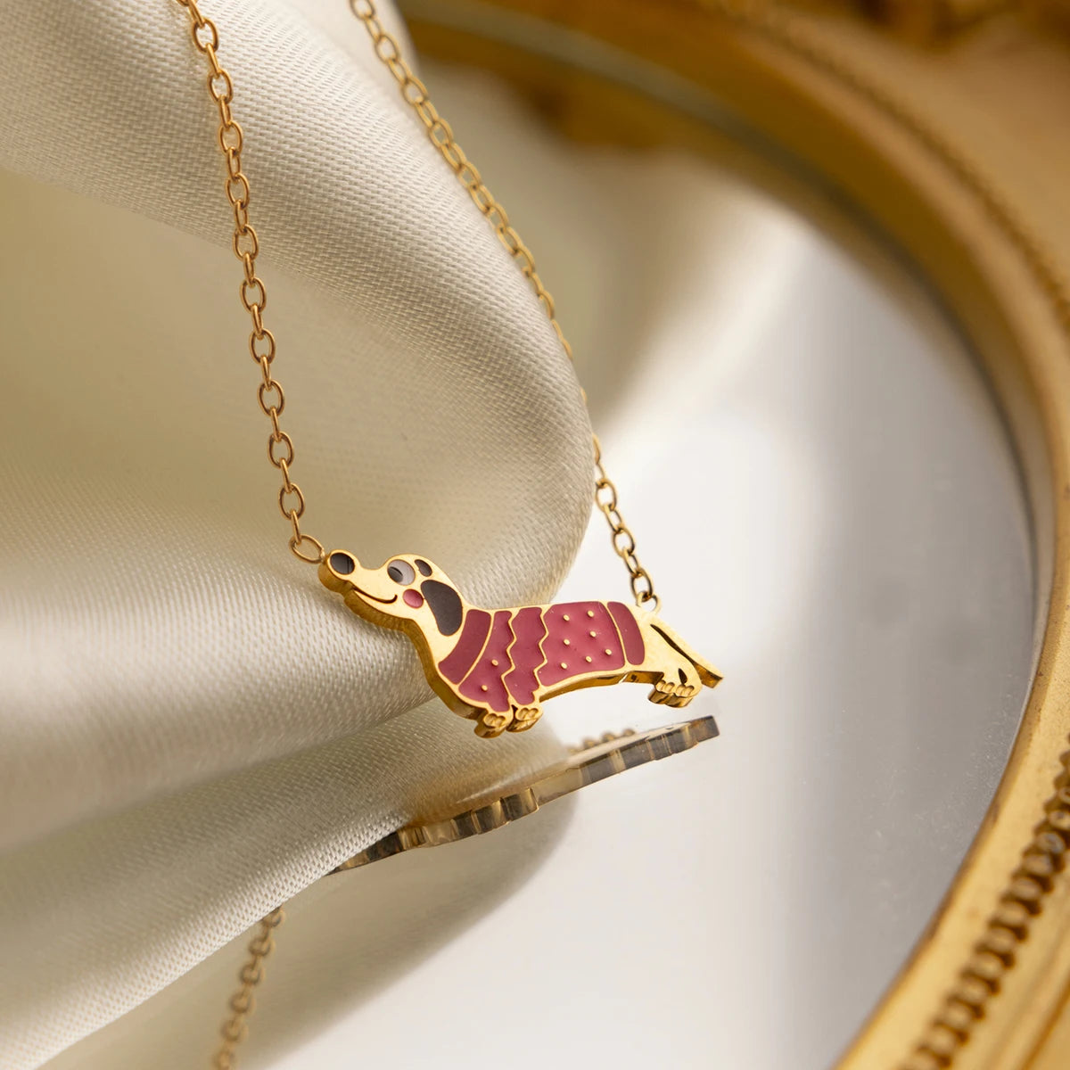 Makroaufnahme des Dackel-Anhängers an einer feinen Goldkette aus Edelstahl; das Design zeigt einen Dackel mit einem rosa gemusterten „Mantel“.