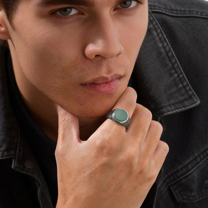 Ein Mann in einer dunklen Denim-Jacke trägt den markanten Vintage-Siegelring mit grünem Stein am Ringfinger.