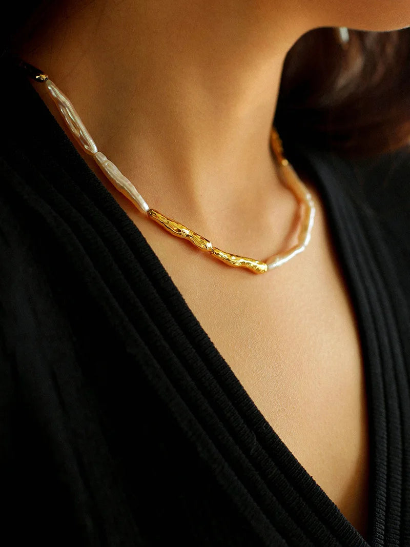 Nahaufnahme einer Frau, die eine moderne Barockperlen-Halskette mit organisch geformten Gold-Details zu einem schwarzen Outfit trägt.