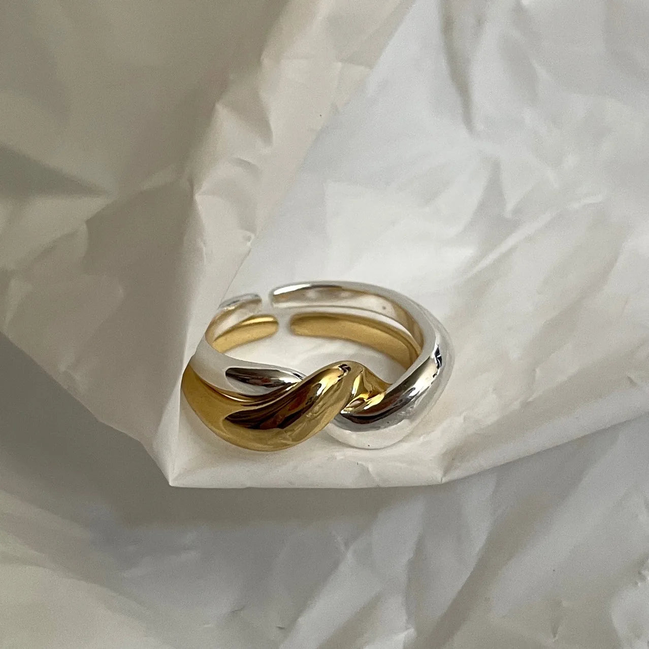 Detail eines hochwertigen Messingrings mit 18 Karat Vergoldung, präsentiert in einem minimalistischen, wellenförmigen Knoten-Design.