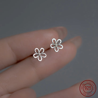 Nahaufnahme von zwei filigranen, blütenförmigen Ohrsteckern aus 925er Sterling Silber auf zwei Fingerspitzen gehalten.