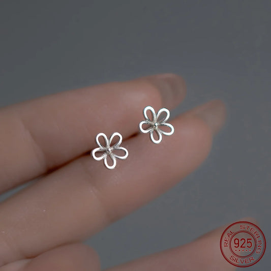 Nahaufnahme von zwei filigranen, blütenförmigen Ohrsteckern aus 925er Sterling Silber auf zwei Fingerspitzen gehalten.