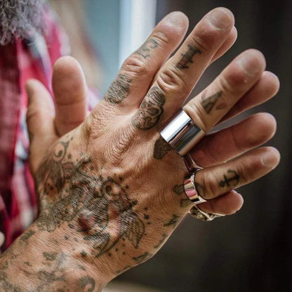 Ein offener, breiter silberner Edelstahlring getragen am Zeigefinger einer stark tätowierten Hand im lässigen Biker-Look.