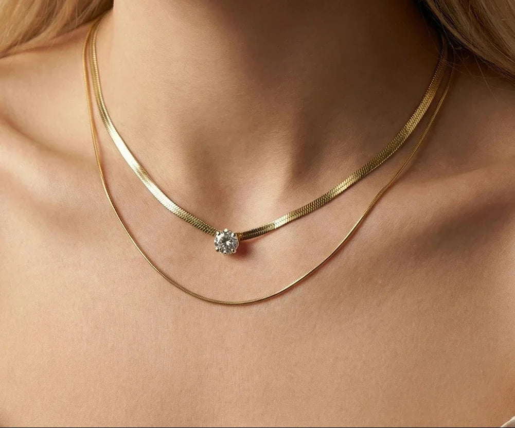 Eine Frau trägt eine zweireihige, vergoldete Edelstahl-Schlangenkette mit einem funkeldem Zirkonia-Stein.