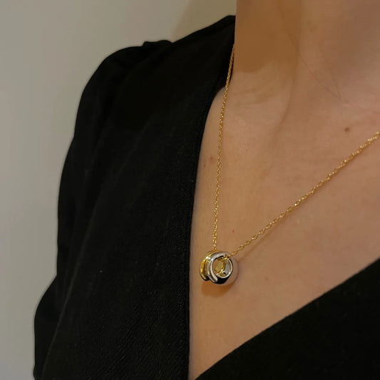 Damen-Halskette aus Messing mit 18K Vergoldung und zwei ineinandergreifenden Ring-Anhängern in Gold und Silber, getragen zu einem schwarzen Oberteil.