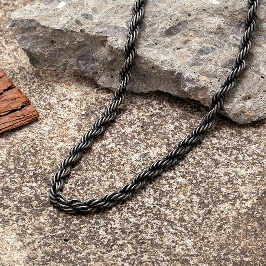 Nahaufnahme der schwarzen, gedrehten Edelstahl-Kordelkette im Vintage-Stil, liegend auf einem hellgrauen, steinernen Untergrund.