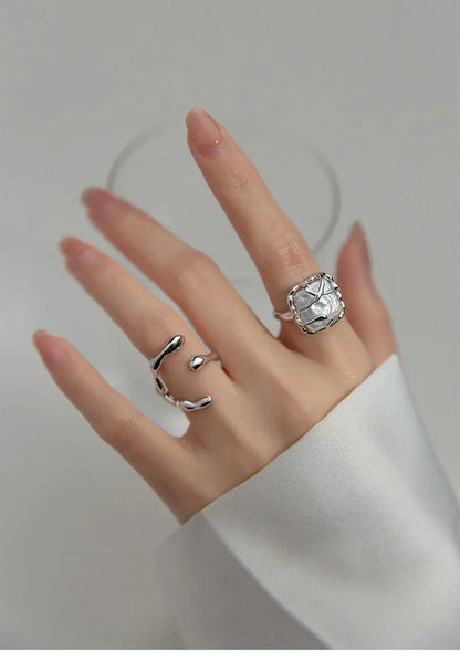 Hand einer Frau mit langen Nägeln, die einen großen, offenen 925er Silberring im Wickel-Design mit einem unregelmäßigen, facettenreichen Stein-Element trägt.