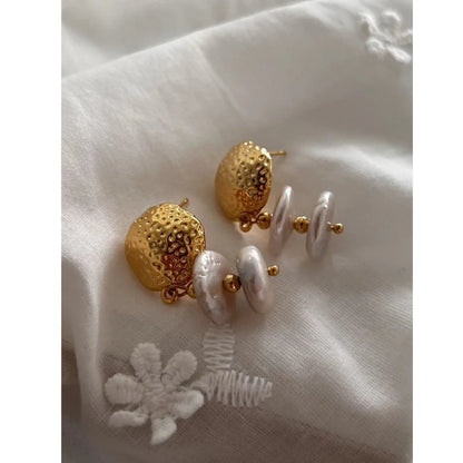 Goldene Ohrringe mit Baroque-Perlen, elegant platziert auf weißem Stoff mit einer weißen, gestickten Blumenapplikation.