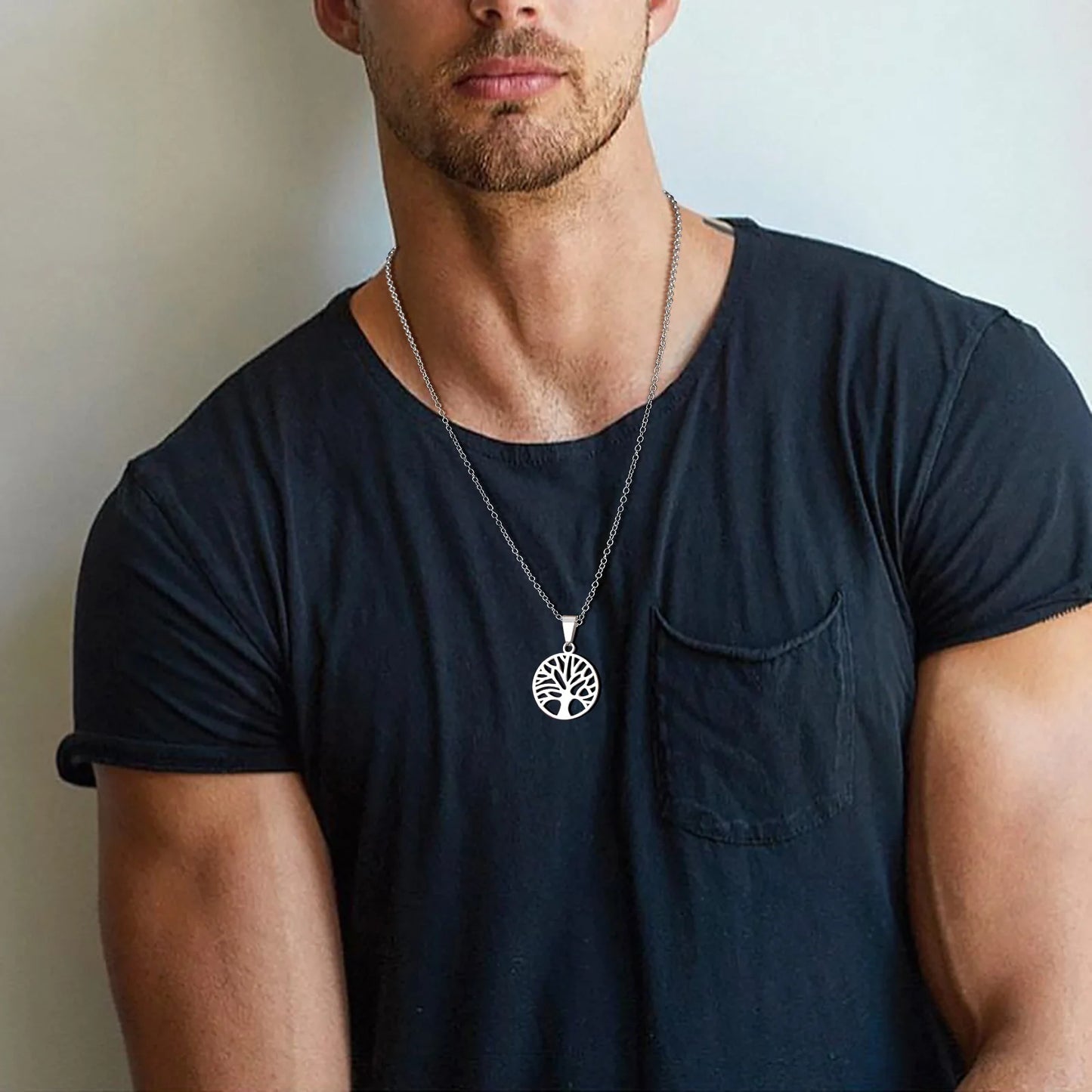 Silberfarbene Edelstahlkette mit Lebensbaum-Medaillon, getragen von einem Mann über einem dunklen T-Shirt, Nahansicht.
