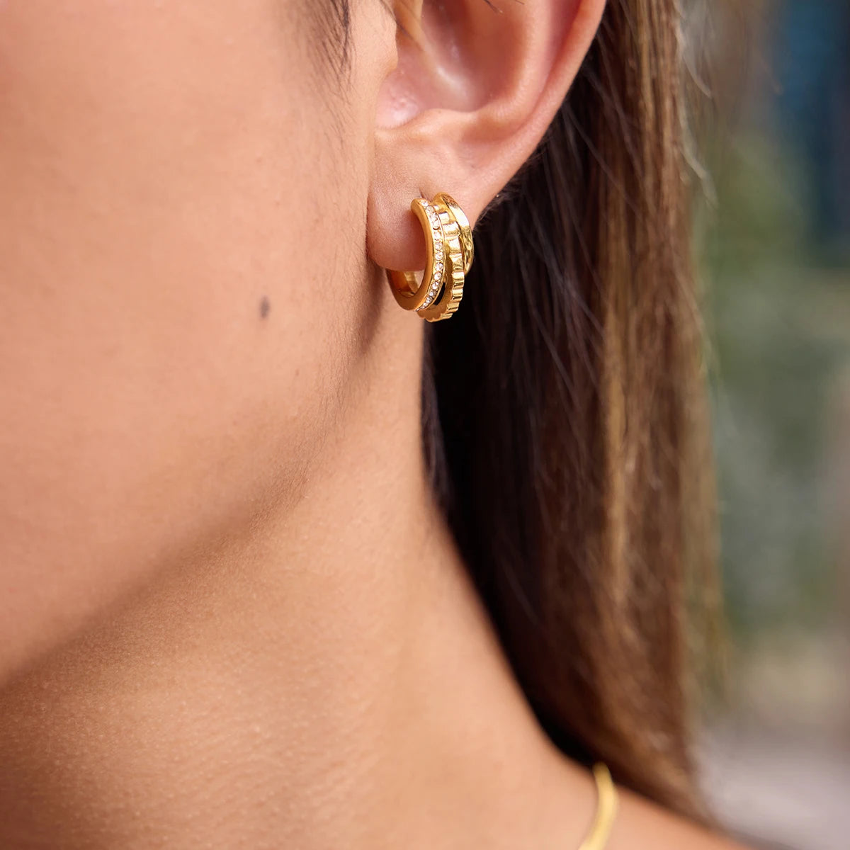 „Nahaufnahme einer Frau, die elegante, dreireihige Creolen aus 18K vergoldetem Edelstahl trägt – eine Reihe ist mit funkelnden Zirkonia-Steinen besetzt.“