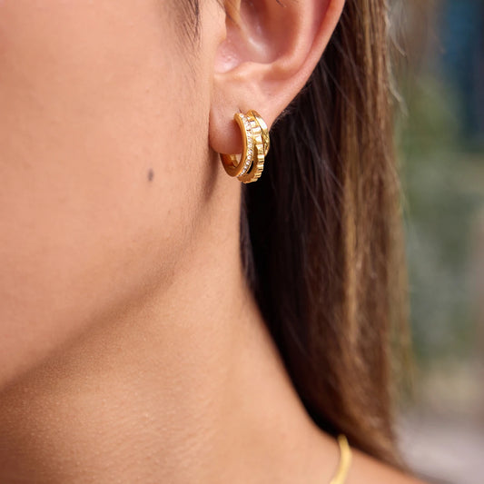 „Nahaufnahme einer Frau, die elegante, dreireihige Creolen aus 18K vergoldetem Edelstahl trägt – eine Reihe ist mit funkelnden Zirkonia-Steinen besetzt.“