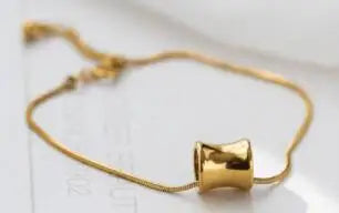 Nahaufnahme des feinen vergoldeten Titan-Armbands mit tailliertem Zylinder-Element auf hellem Untergrund.