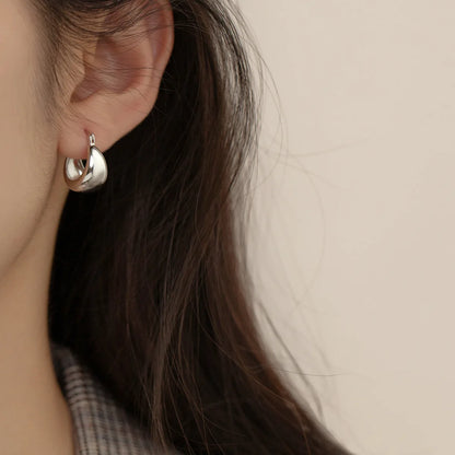 Nahaufnahme eines Ohrs, das einen kleinen, glänzenden, bauchigen Creolen-Ohrring (Huggie-Ohrring) aus 925er Silber trägt.