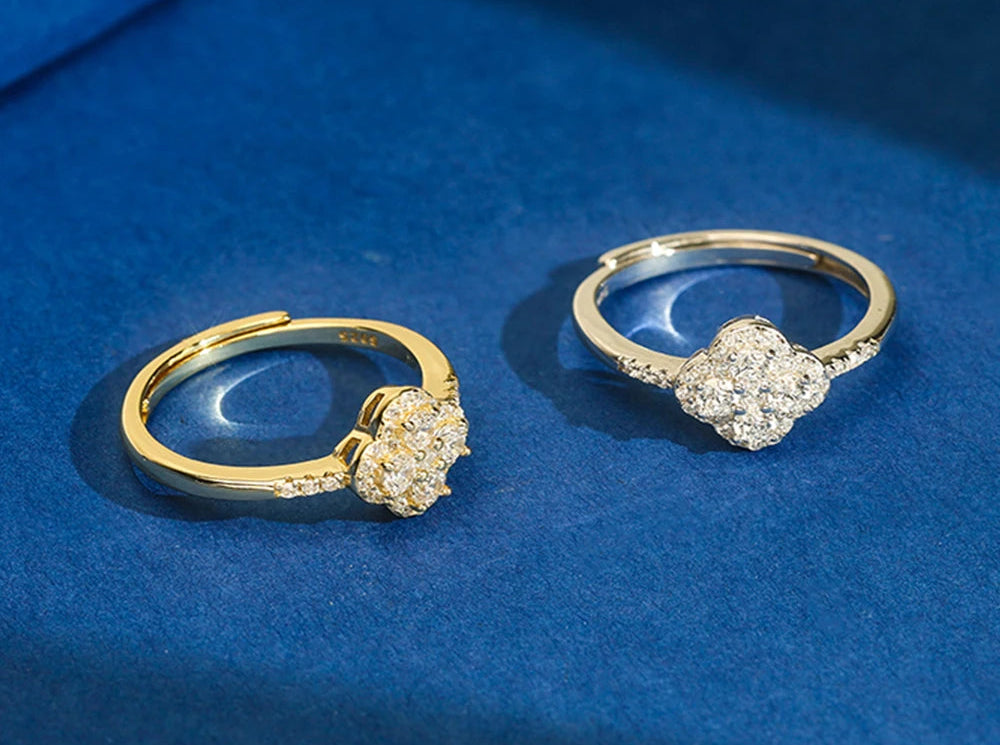 Zwei goldfarbene Ringe mit Kleeblatt-Motiv, besetzt mit Zirkonia , präsentiert vor blauem Hintergrund.