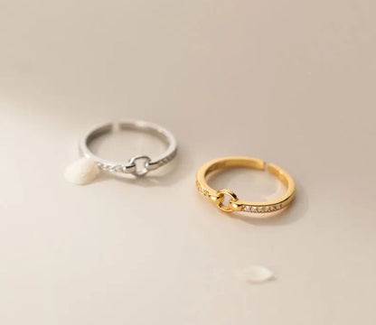 Minimalistisches Produktfoto: Der verstellbare Knoten-Ring in Silber und Gold nebeneinander auf einem beigefarbenen Hintergrund.