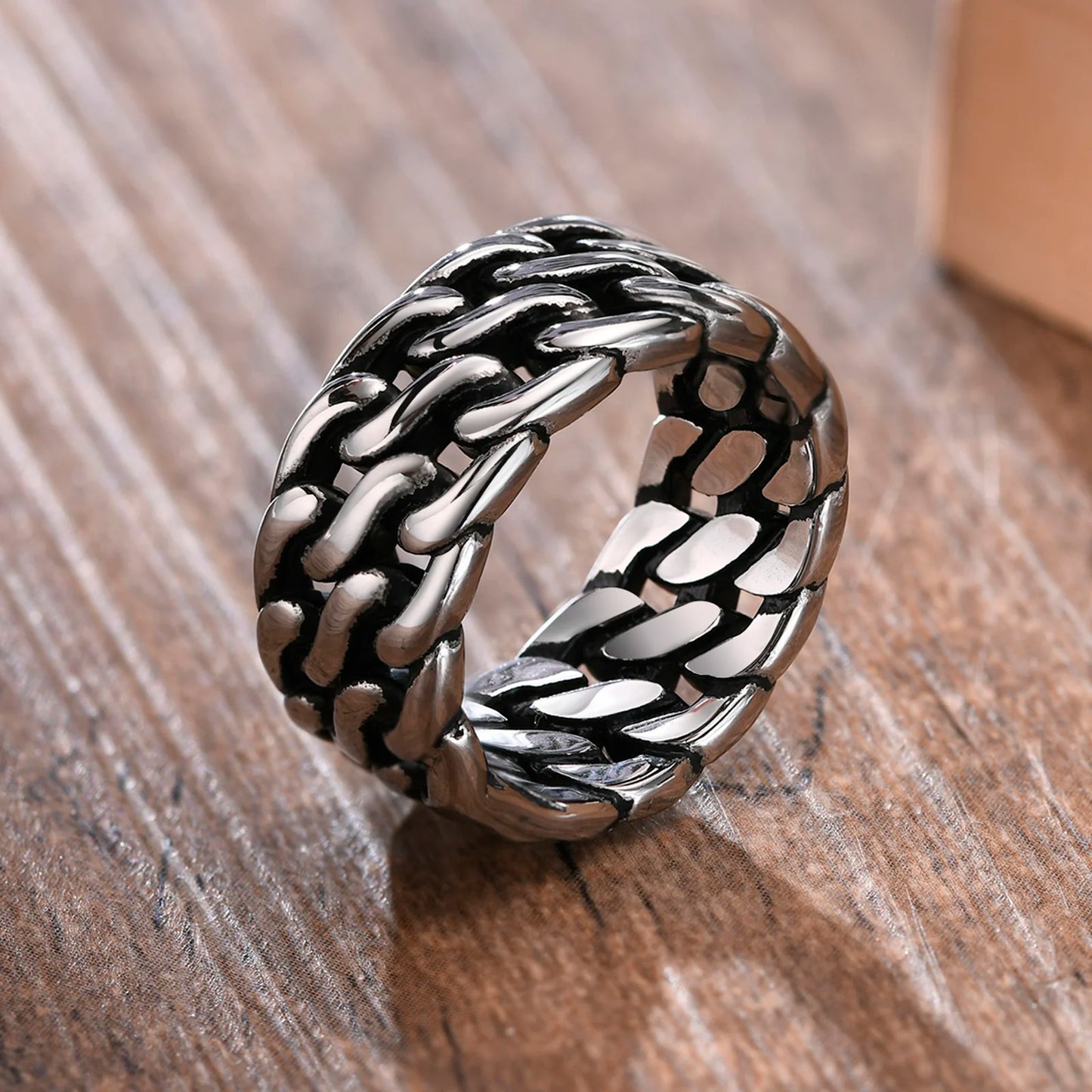 Freigestellter, breiter Edelstahl-Panzerketten-Ring (Silber) in einer leicht gekippten Ansicht auf einem Holzuntergrund.